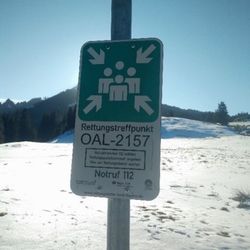Grünes Schild „Rettungstreffpunkt OAL-2157, Notruf 112“ in einer Schneelandschaft